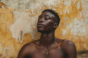 Thoughtful young man with a serene expression poses barechested against a textured, aged wall