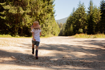 A little girl is standing on the road, near the forest. Day, tourism with children. Nature walks.