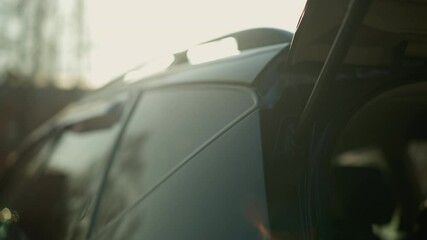 Close-up view of a black car with its trunk being opened, set against a softly blurred outdoor background