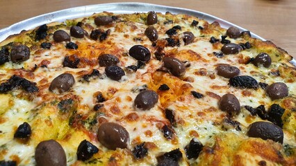 Whole Pizza with Cheese, Whole Black and Brown Olives, and Tomato Sauce on Round Tray on Wooden Table