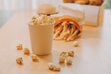 A bucket of popcorn, top-view, warm colors, light brown wooden background, flat lay, daylight macro close-up