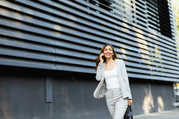 Confident business woman enjoying a sunny day while walking outdoors and chatting on the phone near a modern building