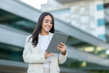 A woman smiles while holding a tablet outside a contemporary building, showcasing a blend of technology and elegant fashion.