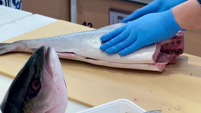 4K Chef skillfully fillets Hamachi fish, with the fish head visible in front of him as he fillets the fish on a cutting board to serve to customers.
