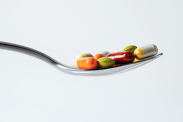 Fototapeta premium A fork holds a variety of colorful pills against a white background.