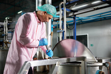 worker stirring water on large industrial pot in the factory