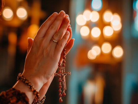 Close-Up of Hands Praying with Rosary Beads in a Church with Candlelight Creating a Peaceful Ambiance