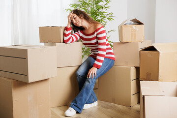 Young woman overwhelmed in her new house surrounded by cardboard boxes that reach the ceiling. Exhausted and stressed young girl opening moving boxes in student rental apartment.