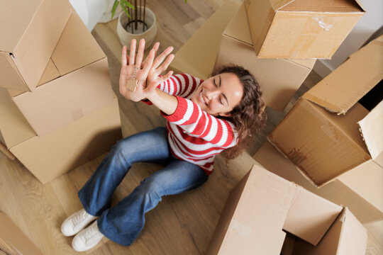 Young woman in her new house surrounded by cardboard boxes, they reach the ceiling. Happy, smiling and excited young girl opening moving boxes in student rental apartment.