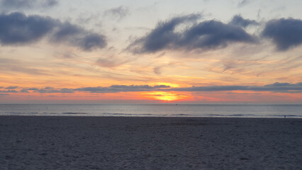 Obraz premium Beach at sunrise with much sand, water and clouds.