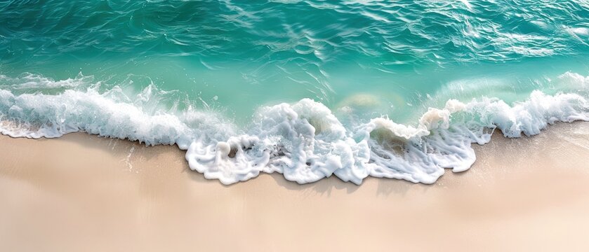 Aerial view of a turquoise ocean wave gently crashing onto a sandy beach, creating a serene and tranquil seaside landscape.