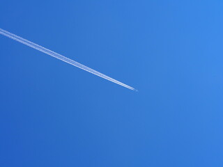 An airplane flies high in the clear blue sky, leaving behind distinct contrails as it moves, depicting freedom and travel, and capturing a moment of serene sky beauty