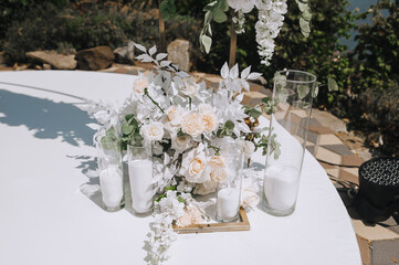 Part, element of decorated wedding arch with flowers, candlesticks standing on white stand outdoors.