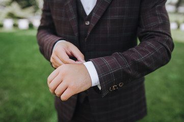 Adult man in brown checkered suit, young businessman, groom buttoning buttons on jacket with hands in the morning. Wedding photography, business concept, getting ready for work.