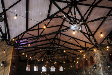 Many electric lamps, glowing garlands hang on the wooden ceiling in the room, in the interior of a modern restaurant. Photography, abstraction, background.