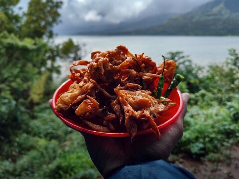 Holding Indian street food kanda bhaji dish having nature scenery in background, favourite Indian snack in monsoon , India