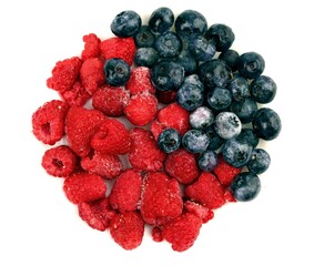 Raspberries and blueberries lying on a plate on a white background. Colorful close-up photo. top view.