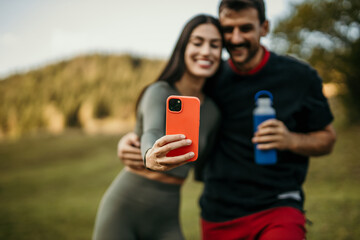 Fototapeta premium Portrait of two sporty smiling young couple after running making selfie outdoors
