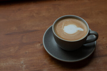 A cup of hot coffee with latte art on wooden table.