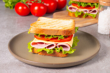 Close-up of two sandwiches with bacon, salami, prosciutto and fresh vegetables on rustic wooden cutting board. Club sandwich concept