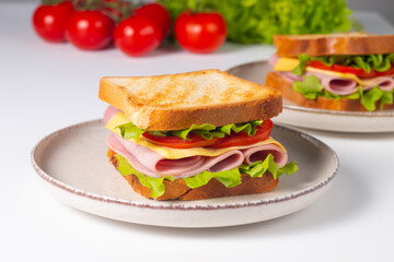 Close-up of two sandwiches with bacon, salami, prosciutto and fresh vegetables on rustic wooden cutting board. Club sandwich concept