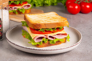 Close-up of two sandwiches with bacon, salami, prosciutto and fresh vegetables on rustic wooden cutting board. Club sandwich concept