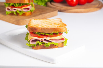 Close-up of two sandwiches with bacon, salami, prosciutto and fresh vegetables on rustic wooden cutting board. Club sandwich concept