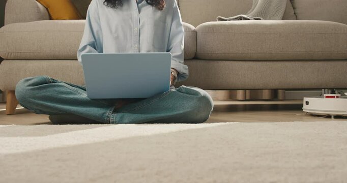 A Modern Home Scene: Woman Types on Laptop as Robot Vacuum Delivers Coffee for a Cozy, Tech-Savvy Moment