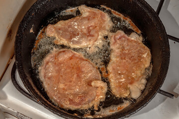 Schnitzel or chops are fried in boiling oil on an old cast iron hot frying pan. Close-up