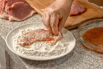 Cook dips pieces of beaten meat fillet in flour before further frying in a frying pan