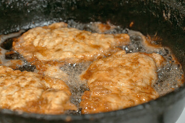 Schnitzel or chops are fried in boiling oil on an old cast iron hot frying pan. Close-up