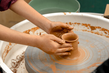 Children's hands create pottery on a potter's wheel during a master class on an outdoor playground