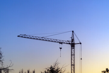 Dark silhouette of tower construction crane after work shift at sunset with soft focus against...