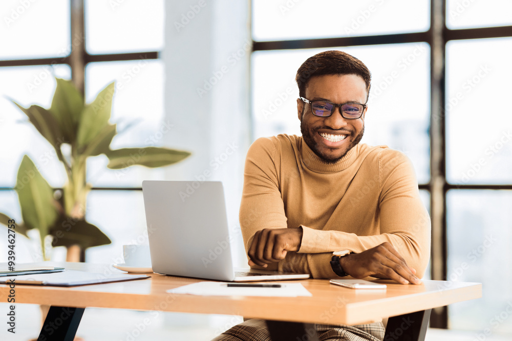Poster blogger at work. smiling black man looking at camera, sitting at desk with laptop. selective focus
