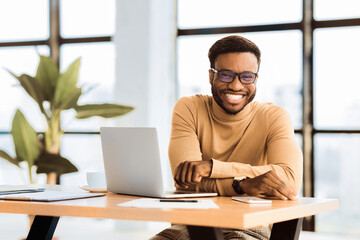 Obraz premium Blogger At Work. Smiling black man looking at camera, sitting at desk with laptop. Selective focus