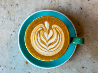 A cup of coffee latte on a marble table. A mug of flat white coffee on a marble background. Coffee art. Heart flower shape latte art. Turquoise cup and saucer