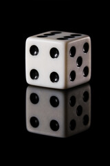 a white six-sided D6 dice with black dots, showing four dots, on a black background with a reflection