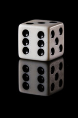 a white six-sided D6 dice with black dots, showing six dots, on a black background with a reflection