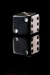 a black six-sided D6 dice with white dots, showing two dots, on a black background with a reflection