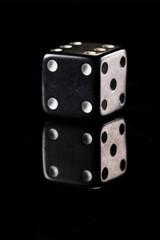 a black six-sided D6 dice with white dots, showing four dots, on a black background with a reflection