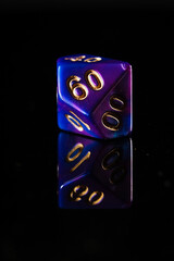 a blue and purple marbled ten-sided D10 dice with gold numbers that show the number sixty, on a black background with a reflection