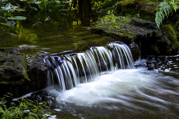 Idyllischer Wasserfall im grünen Wald mit dunklen Felsen und Moos - lange Belichtung © Patrick Hirschi