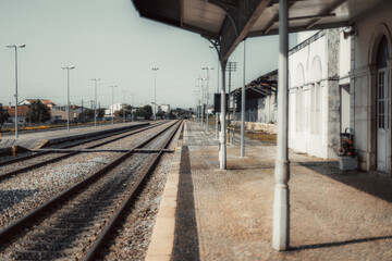 An empty, quiet railway station with multiple tracks leading into the distance. The platform is...