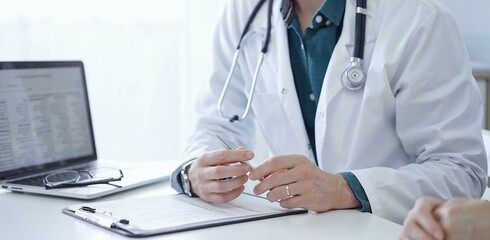 Doctor and a patient. The physician, wearing a white medical coat over a green shirt, is gesturing with his hands during a consultation in the clinic. Medicine
