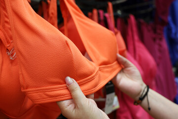 Woman chooses orange swimsuit hanging on rack in lingerie store. Concept of shopping, customer...