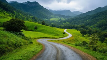 Fototapeta premium Wide view of a picturesque, winding road through a lush green landscape with scenic mountains in the distance