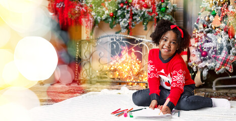 Fototapeta premium Portrait of cute little black girl sitting on floor, drawing near Christmas tree, writing letter to Santa, preparing wish list of Xmas presents