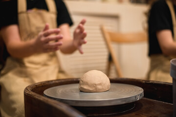 Potter girl works on potter's wheel, making ceramic pot out of clay in pottery workshop