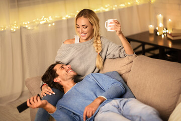 Loving couple drinking tea and enjoying winter holidays, talking and watching tv on sofa