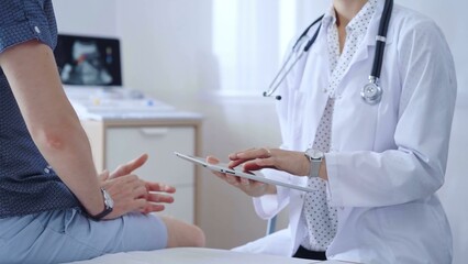 Doctor woman is taking notes on a tablet computer while a male patient describes his symptoms in clinic procedure cabinet. Medicine service concept